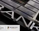 Litery "BANK" na fasadzie budynku, odbijające się w szklanej elewacji.